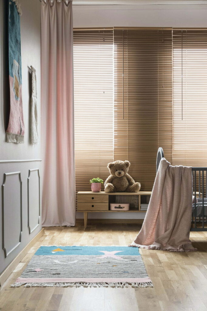 Pink blanket on bed and rug in bright baby's room interior with